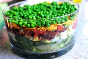 Une salade étagée colorée parfaite pour les repas-partage et les pique-niques. C'est une salade printanière simple et belle, et un aliment de base des repas-partage et des déjeuners dans ma région du pays. Vous pouvez varier les ingrédients selon vos goûts et ce que vous avez dans votre frigo, et vous pouvez l'agrémenter un peu d'herbes fraîches, de gorgonzola, tout ce qui fait voler votre jupe ! Les ingrédients standard de la plupart des salades en couches sont de la laitue ou des épinards (ou les deux !), Des œufs durs, du bacon émietté, du fromage râpé, des oignons verts et des pois verts, qui sont disposés en couches dans un joli bol en verre afin que les couches puissent être vues dans tous les sens. leur beauté colorée.